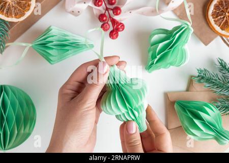 Les mains féminines déplient des ornements en nid d'abeille de Noël en papier. Décoration sans plastique pliable faite à la main. Concept d'artisanat de créativité hivernale. Mode éco DIY. SC Banque D'Images