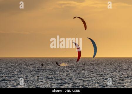 Trois des kitesurfers au coucher du soleil en face de la plage de Fremantle, Australie occidentale Banque D'Images
