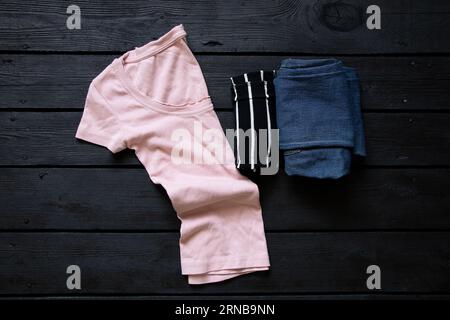 T-shirt rose et jeans et t-shirt reposent sur une planche en bois noir, mode et style, plat Banque D'Images