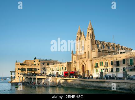 Vue sur l'église historique 'St. Julian' sur Malte. La cathédrale est sur la côte et se reflète dans la mer. Au premier plan une rue avec un tour Banque D'Images