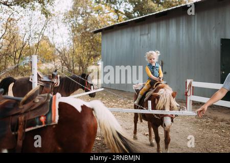 Petite fille étant conduite sur poney tour à la ferme familiale Banque D'Images