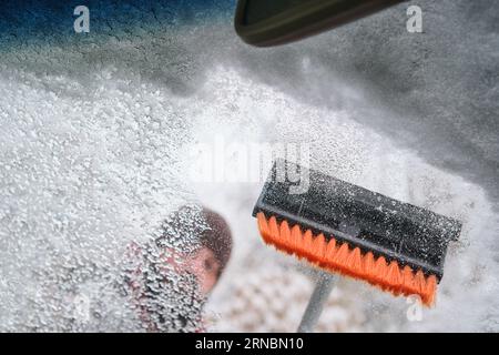 A man cleans the ice from the windshield of a car with a brush, Stock Photo