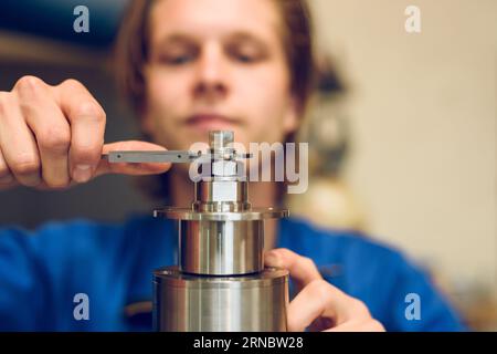Jeune homme de récolte concentré serrant la vis de la machine dans l'usine floue Banque D'Images