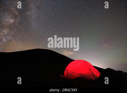 Tente éclairée par la lumière rouge sous la voie lactée et ciel étoilé de nuit au sommet de la montagne Banque D'Images