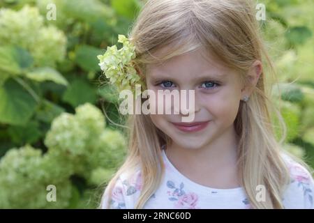 Portrait extérieur candide de petite fille heureuse avec fleur verte derrière son oreille Banque D'Images