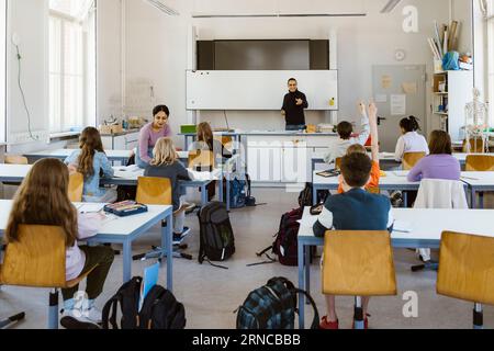 Enseignant masculin et féminin enseignant les étudiants assis sur un banc dans la salle de classe Banque D'Images