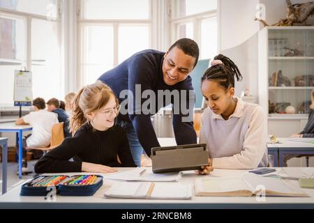 Enseignant masculin souriant faisant E-learning avec des étudiantes en classe Banque D'Images