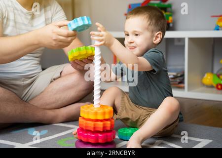 Heureux souriant petit garçon en bas âge 2,5 ans jouant pyramide colorée avec papa. Passer du temps avec les enfants. Jouets éducatifs pour enfants. Chambre d'enfants. Banque D'Images