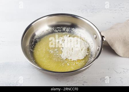 Flour is added to melted butter in a frying pan on a light gray background. Making cheese pasta sauce, step by step, do it yourself, step 2. Stock Photo