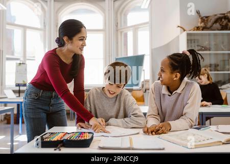 Professeur heureux regardant l'étudiante tout en aidant dans la salle de classe Banque D'Images