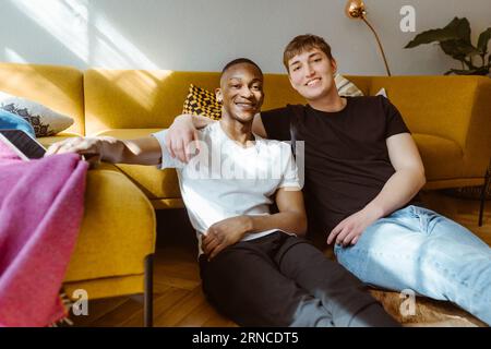 Portrait de jeune homme souriant assis avec le bras autour d'un ami à la maison Banque D'Images