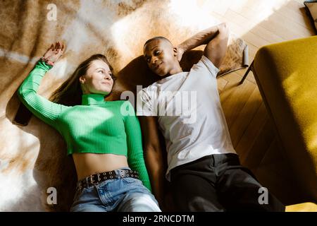 Vue à grand angle de la femme souriante couchée sur le sol par un ami masculin à la maison Banque D'Images