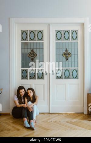 Tristes amis assis sur le sol ensemble contre la porte blanche à la maison Banque D'Images