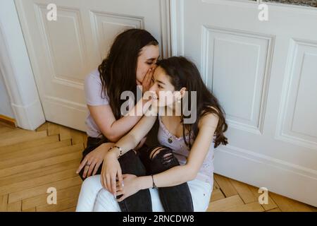 Jeune femme chuchotant à une amie contre la porte blanche à la maison Banque D'Images