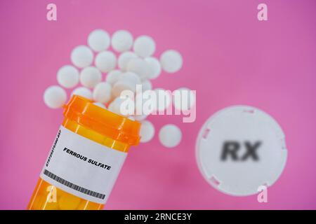 Sulfate ferreux Rx pilules de médecine dans un flacon plactique avec des comprimés. Pilules renversant du récipient jaune sur fond rose. Banque D'Images