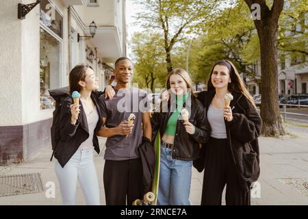 Portrait de jeunes amis souriants mangeant des glaces sur le trottoir Banque D'Images