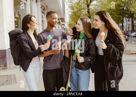 Heureux jeunes amis mangeant des glaces au trottoir Banque D'Images