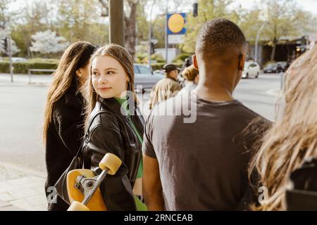 Jeune femme regardant en arrière tout en marchant avec des amis dans la ville Banque D'Images