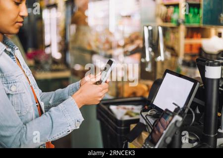 Femme utilisant un téléphone intelligent tout en scannant le code QR pour le paiement à la caisse du magasin Banque D'Images