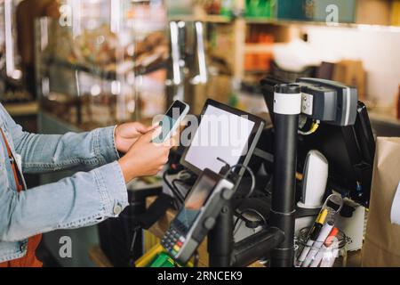 Section médiane de la femme à l'aide d'un téléphone intelligent tout en scannant le code QR pour le paiement à la caisse du magasin Banque D'Images