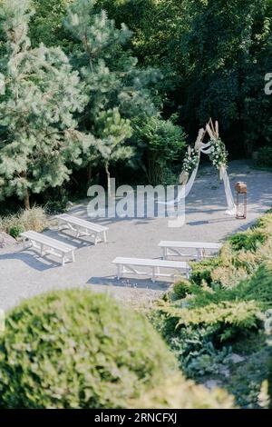 Cérémonie de mariage dans le magnifique jardin paysager avec arc de mariage élégant décoré de roses blanches fraîches et des bancs blancs à côté. Vue de dessus. Banque D'Images