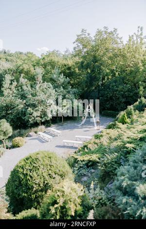 Cérémonie de mariage dans le magnifique jardin paysager avec arc de mariage élégant décoré de roses blanches fraîches et des bancs blancs à côté. Vue de dessus. Banque D'Images