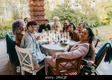 Portrait d'amis heureux de la communauté LGBTQ assis à la table à manger pendant le dîner dans la cour arrière Banque D'Images