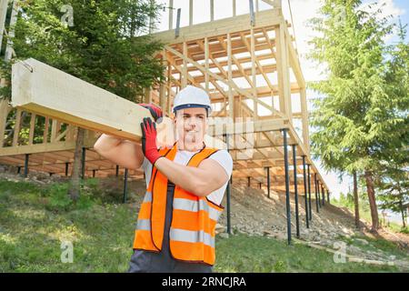 Constructeur, travailleur portant uniforme et casque snording, tenant dorure en bois, planche, transport. Banque D'Images