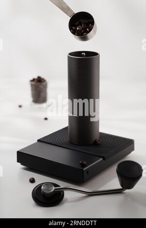 Utilisez une cuillère en acier inoxydable pour ramasser les grains de café dans un moulin à café manuel sur une balance numérique noire. Banque D'Images
