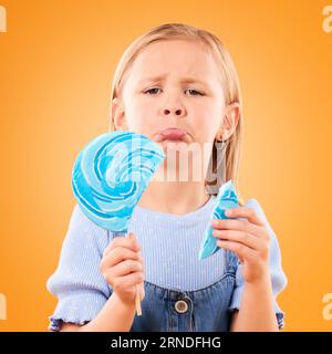 Portrait, enfants et fille triste avec une sucette cassée sur un fond orange en studio à l'air contrarié. Enfants, bonbons et malheureux avec une fille Banque D'Images