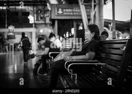 Dans cette photographie en noir et blanc, une femme thaïlandaise âgée est assise contemplativement sur un banc d'attente à la gare de Hua Lamphong à Bangkok, en Thaïlande Banque D'Images