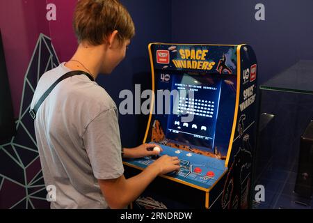 Machine de jeu Taito envahisseurs de l'espace. Simple Space Arcade dans le vieux jeu vidéo rétro 8 bits. Garçon joue à la machine à sous classique. Varsovie, Pologne - 28 juillet 2023. Banque D'Images