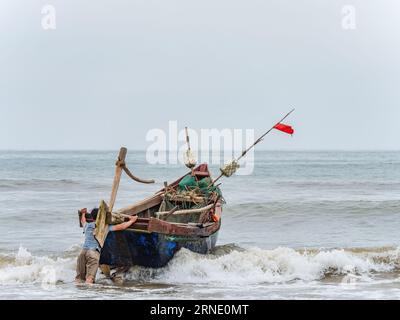 Pêcheur lançant son bateau contre le vent et les hautes vagues à Sam son Beach, Thanh Hoa, Vietnam Banque D'Images