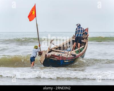 Deux personnes lançant leur bateau contre le vent et les hautes vagues à Sam son Beach, Thanh Hoa, Vietnam Banque D'Images