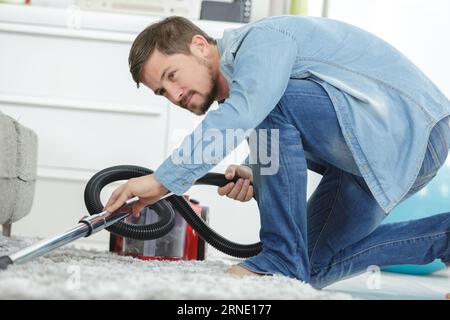 homme aspirant un sol sous un canapé Banque D'Images