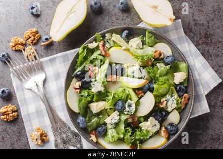 Salade gourmande avec poires douces, bleuets, fromage bleu, laitue et noix en gros plan dans une assiette sur la table. Vue de dessus horizontale Banque D'Images