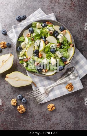 Salade d'automne composée de poires mûres, bleuets, fromage bleu, laitue et noix gros plan dans une assiette sur la table. Vue verticale de dessus Banque D'Images