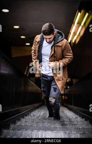 l'homme marche lentement sur les marches vers le haut du métro à la ville tout en se tenant sur les escaliers électriques regarder de côté Banque D'Images