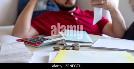 L'homme est frustré de ses factures de vie et de les calculer devant son canapé dans le salon Banque D'Images