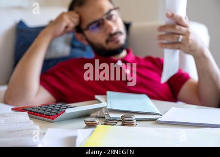 L'homme est frustré de ses factures de vie et de les calculer devant son canapé dans le salon Banque D'Images