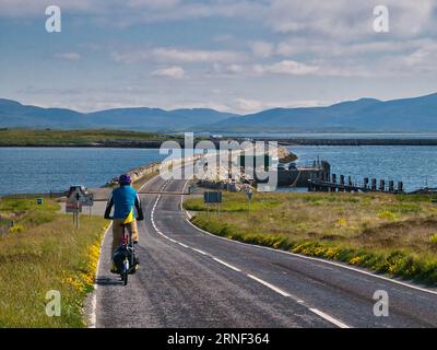 Par une journée claire et ensoleillée, un seul cycliste se dirige vers la chaussée reliant les îles de North Uist et Berneray dans les Hébrides extérieures, en Écosse, au Royaume-Uni. Banque D'Images