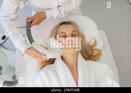 Cliché recadré des mains cosméticienne méconnaissable effectuant une procédure de cosmétologie de rajeunissement de photo pour la femme dans la clinique de beauté moderne. Banque D'Images