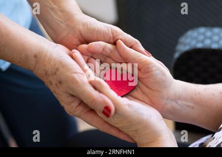 Morceau d'Un coeur rouge dans les mains d'une femme âgée à côté de sa fille. Le concept d'amour et de soins pour les personnes âgées. Gros plan Banque D'Images