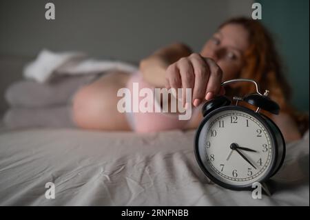 Une femme enceinte se couche dans son lit et tient un réveil. Banque D'Images