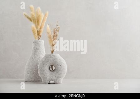 Vases décoratifs en pierre de lave avec des fleurs sèches sur fond clair Banque D'Images