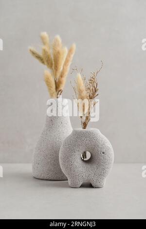 Vases décoratifs en pierre de lave avec des fleurs sèches sur fond clair Banque D'Images