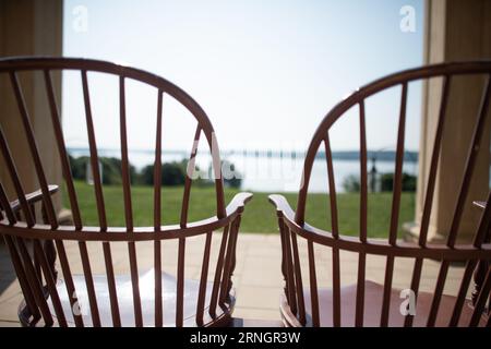 MOUNT VERNON, Virginie - les chaises Windsor traditionnelles en bois bordent la célèbre piazza à colonnades du manoir Mount Vernon de George Washington. Les chaises, peintes en vert pour correspondre aux volets, sont orientées vers l'extérieur vers la pelouse étendue et la rivière Potomac au-delà. Ce porche historique reflète le style de vie du XVIIIe siècle du premier président américain. Banque D'Images