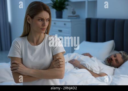 Femme irritée assise sur le lit à la maison, espace pour le texte. Problème avec le mari ronflant Banque D'Images