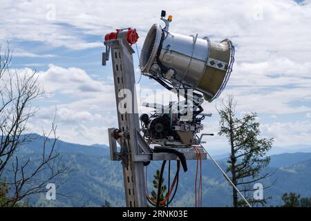 Canon à neige jaune sur le bord d'une colline surplombant la vallée en été Banque D'Images