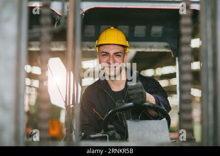 Portrait conducteur heureux de chariot élévateur portant le casque de sécurité et le gilet aiment travailler transportant des marchandises dans la cargaison d'expédition d'entrepôt Banque D'Images